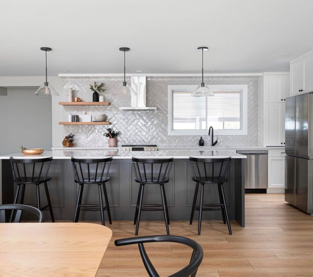 Modern kitchen from Stone Design Concepts Gallery featuring a large island with dark cabinetry, black bar stools, and sleek herringbone tile backsplash.